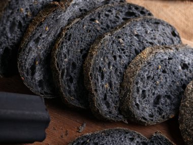 Tahtada dilimlenmiş taze pişmiş siyah kömür hamurlu ciabatta ekmeği.