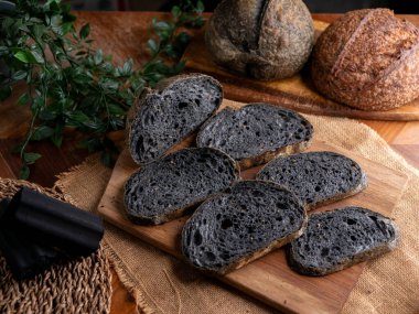 Tahtada dilimlenmiş taze pişmiş siyah kömür hamurlu ciabatta ekmeği.