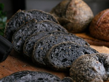 Tahtada dilimlenmiş taze pişmiş siyah kömür hamurlu ciabatta ekmeği.