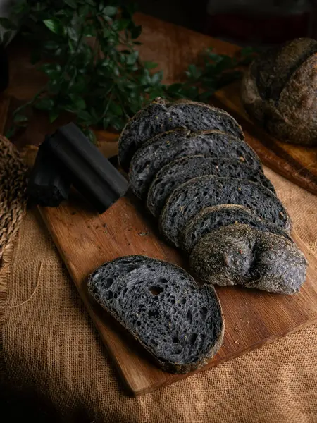 Tahtada dilimlenmiş taze pişmiş siyah kömür hamurlu ciabatta ekmeği.