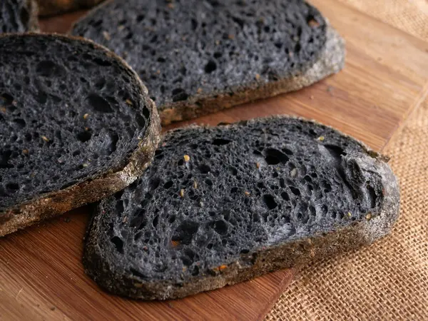 Tahtada dilimlenmiş taze pişmiş siyah kömür hamurlu ciabatta ekmeği.