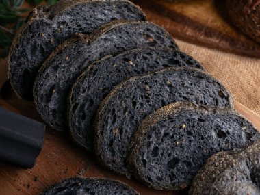 Tahtada dilimlenmiş taze pişmiş siyah kömür hamurlu ciabatta ekmeği.