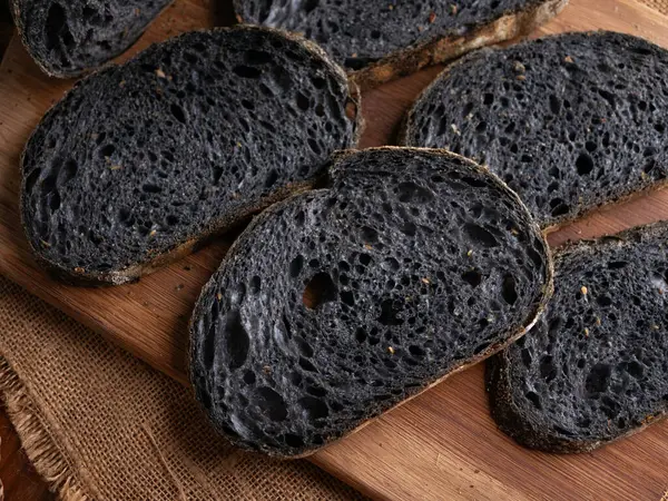 Tahtada dilimlenmiş taze pişmiş siyah kömür hamurlu ciabatta ekmeği.