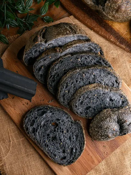 Tahtada dilimlenmiş taze pişmiş siyah kömür hamurlu ciabatta ekmeği.