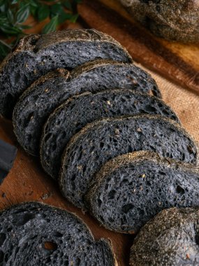 Tahtada dilimlenmiş taze pişmiş siyah kömür hamurlu ciabatta ekmeği.