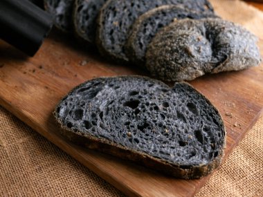 Tahtada dilimlenmiş taze pişmiş siyah kömür hamurlu ciabatta ekmeği.
