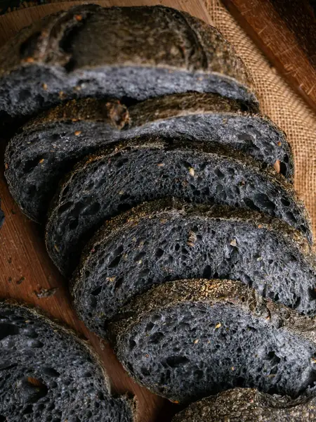 Tahtada dilimlenmiş taze pişmiş siyah kömür hamurlu ciabatta ekmeği.