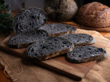 Tahtada dilimlenmiş taze pişmiş siyah kömür hamurlu ciabatta ekmeği.