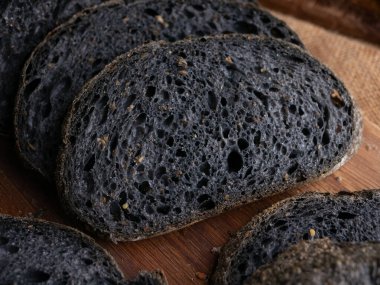 Tahtada dilimlenmiş taze pişmiş siyah kömür hamurlu ciabatta ekmeği.