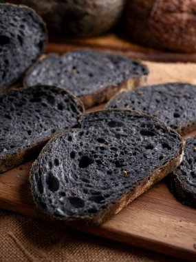 Tahtada dilimlenmiş taze pişmiş siyah kömür hamurlu ciabatta ekmeği.