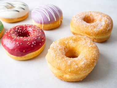 Beyaz arkaplanda farklı renklerde krema tasarımları olan çörekler.