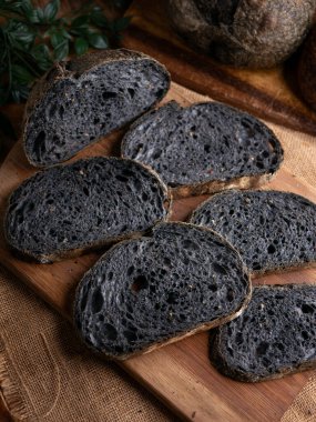 Tahtada dilimlenmiş taze pişmiş siyah kömür hamurlu ciabatta ekmeği.