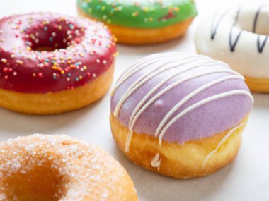 Beyaz arkaplanda farklı renklerde krema tasarımları olan çörekler.