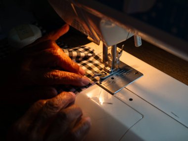 Yaşlı kadın elleri elektrikli dikiş makinesiyle kumaş dikiyor. Kıdemli İşçi ve El Sanatları.