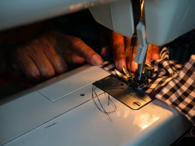 Yaşlı kadın elleri elektrikli dikiş makinesiyle kumaş dikiyor. Kıdemli İşçi ve El Sanatları.
