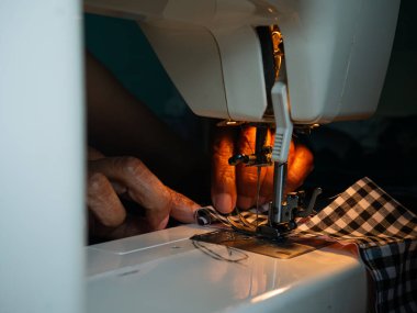 Yaşlı kadın elleri elektrikli dikiş makinesiyle kumaş dikiyor. Kıdemli İşçi ve El Sanatları.