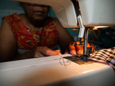 Yaşlı kadın elleri elektrikli dikiş makinesiyle kumaş dikiyor. Kıdemli İşçi ve El Sanatları.