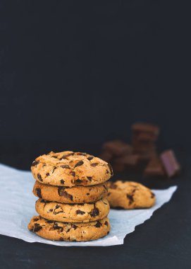 Parşömen üzerinde çikolatalı kurabiyeler ve siyah arka planda çikolata parçaları. 