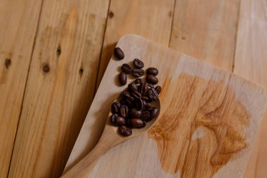 Dark Roasted coffee beans in wooden spoon on wooden board.