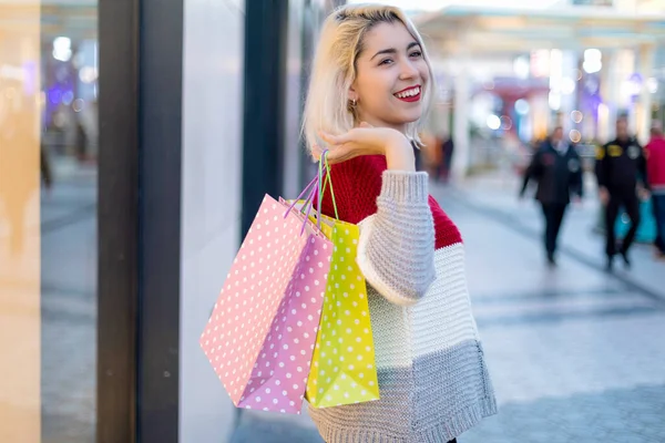 ショッピングモールの隣に立っている間 ブロンドの笑顔の女性はショッピングバッグを保持 — ストック写真