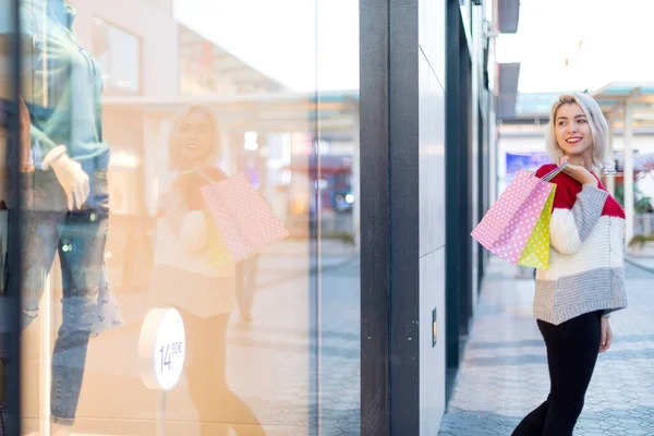 ショッピングモールの隣に立っている間 ブロンドの笑顔の女性はショッピングバッグを保持 — ストック写真