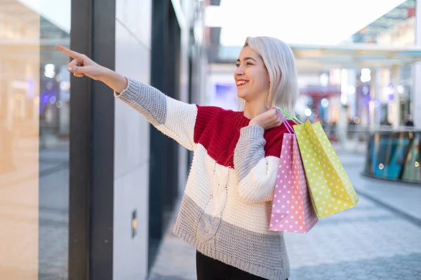 年轻快乐微笑的女人的画像 她提着购物袋指向街上的购物中心 — 图库照片