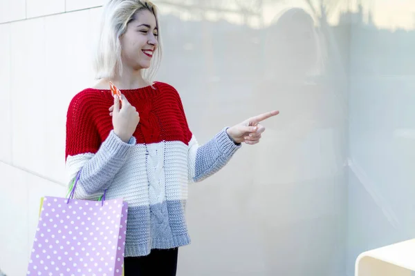 年轻快乐微笑的女人的画像 她提着购物袋指向街上的购物中心 — 图库照片