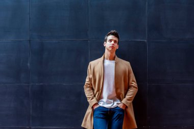 Sokağın ortasında kış giysileri giyen genç adam. Ceket, kot ve beyaz tatlı ile modern saç modeli ile genç adam.