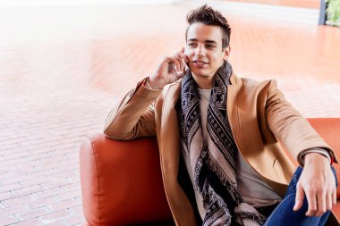 Sokağın ortasında kış giysileri giyen genç adam. Ceket, atkı, mavi kot pantolon ve beyaz tatlı ile modern saç modeli ile genç adam.