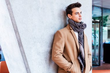 Sokağın ortasında kış giysileri giyen genç adam. Ceket, kot ve beyaz tatlı ile modern saç modeli ile genç adam.