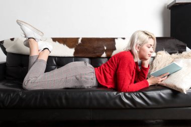 Çekici genç bir kadın evde vakit geçiriyor. Kitapla kanepede uzanmak.