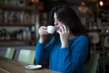 Beautiful woman is drinking delicious coffee while sitting in the bar while talking by phone