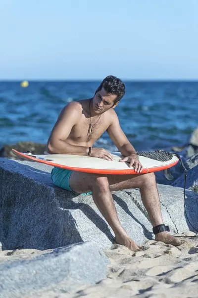 Een Serieuze Man Zittend Rotsen Met Surfplank Stockfoto