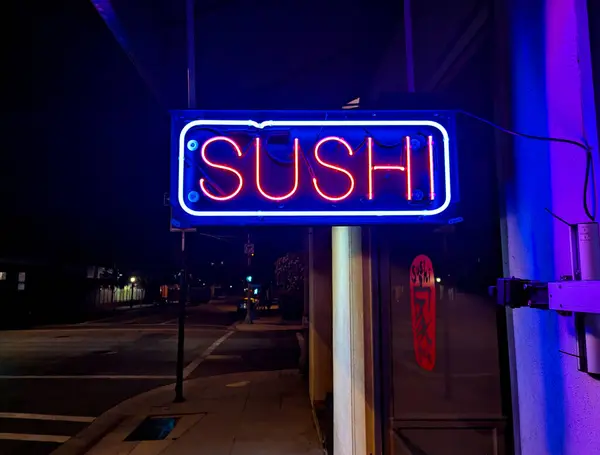 Sıcak bir yaz akşamında parlayan bir Japon restoranının önündeki neon suşi tabelası.. 