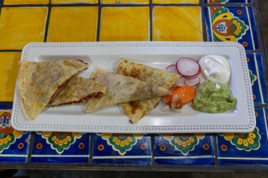 Lezzetli bir Al Pastor quesadilla tabağında ekşi krema ve yanında guacamole.