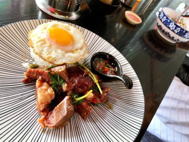 Tayland yemeği, fesleğen kıymalı domuz eti, ahşap masa arkasında pilav üzeri kızarmış yumurta.