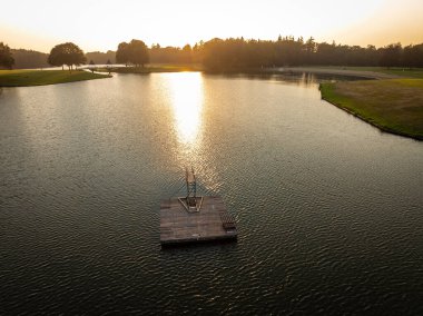 Gün batımında yüzen bir gölün üzerinde dalış kulesi olan ahşap yüzer platform