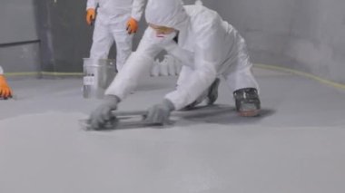 The builder smoothes the surface of the floor with a spatula. A builder in a protective suit creates a polymer floor.