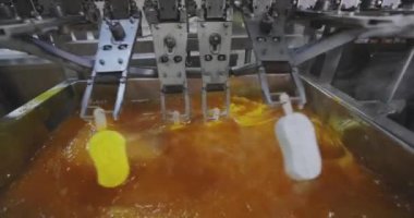 Ice cream is dipped into a container with fruit glaze. Colorful bright ice cream on the conveyor. Ice cream production.
