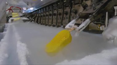 Ice cream is dipped into a container with fruit glaze. Colorful bright ice cream on the conveyor. Ice cream production.