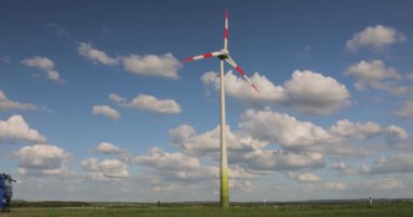 Bulutlu mavi gökyüzüne karşı yeşil bir alanda rüzgar türbini. Rüzgâr jeneratörü devrede. Rüzgâr türbinlerinin gökyüzüne karşı dönüşü.