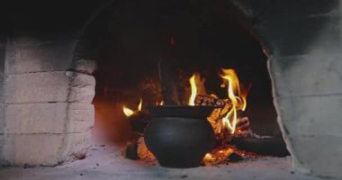 Yanan bir odun fırınında kazan. Yanan bir odun sobasına demir kazanı dök. Eski odun sobası. Yemek pişiyor ama fırında yanıyor..