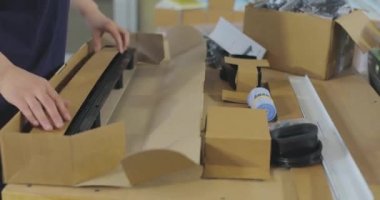 Kadın paketleyici ürünü bir kutuya koyar. Malları bir kutuya koymak. Paketçi fabrikada çalışıyor..