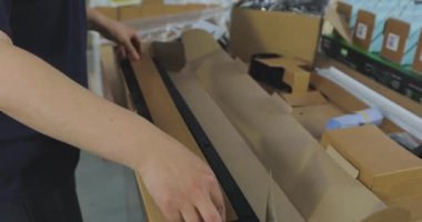 Kadın paketleyici ürünü bir kutuya koyar. Malları bir kutuya koymak. Paketçi fabrikada çalışıyor..