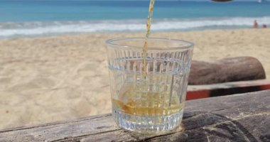 Alkol sahilde bir bardağa dökülür. Viski bardağa dökülür. Viski, sahilin arka planına karşı bardağa dökülür.