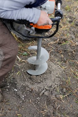 Kasım ayında çamurlu toprağa ağaç dikerken elle tutulan toprak delme makinesi kullanan bir adamla ilgili detaylar (seçici odak).