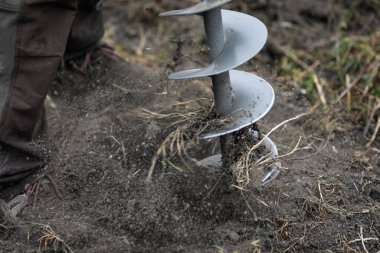 Kasım ayında çamurlu toprağa ağaç dikerken elle tutulan toprak delme makinesi kullanan bir adamla ilgili detaylar (seçici odak).