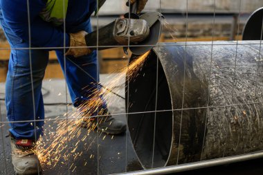 Endüstriyel metalik boru hattında bir açı öğütücü kullanan bir işçiyle sığ alan derinliği (seçici odak) ayrıntıları.