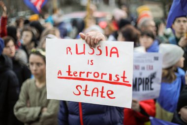 Bucharest, Romania - February 24, 2023: Shallow depth of field (selective focus) image with the hand of a man holding an anti war in Ukraine banner during a protest.