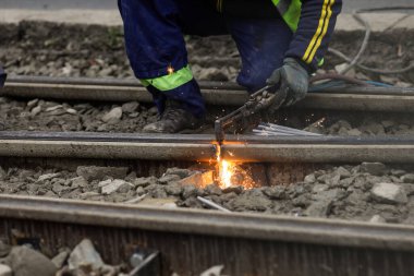 Metal tramvay raylarını kesmek için oksi-asetilen meşalesi kullanan bir işçiyle ilgili detaylar.